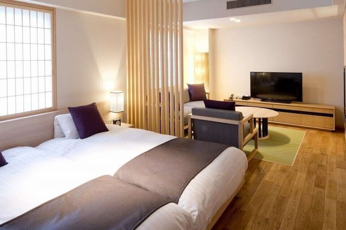 A hotel room with two beds, a TV, a desk, and a sliding door.