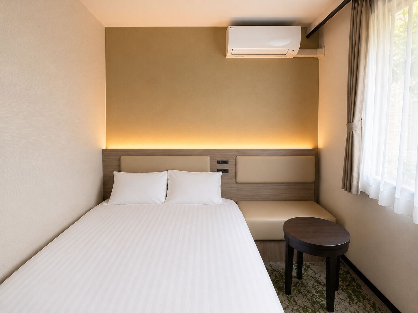 Una habitación de hotel con cama, mesita de noche y unidad de aire acondicionado.