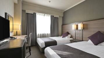 A hotel room with two beds, a desk with a computer, a TV, and a window with curtains.