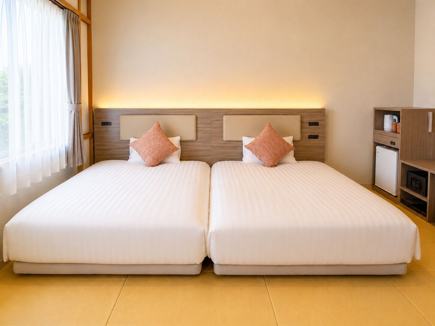 A double bed with a headboard, two pillows, a bedside table with a lamp, and a small refrigerator.