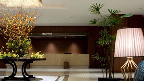 A reception area with a reception desk, a decorative plant arrangement, a floor lamp, and a seating area with a blue chair.