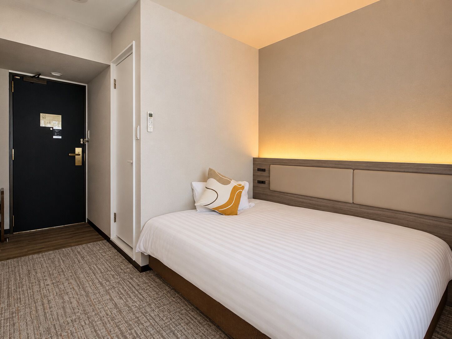 Una habitación de hotel con cama, puerta y una lámpara fijada a la pared.