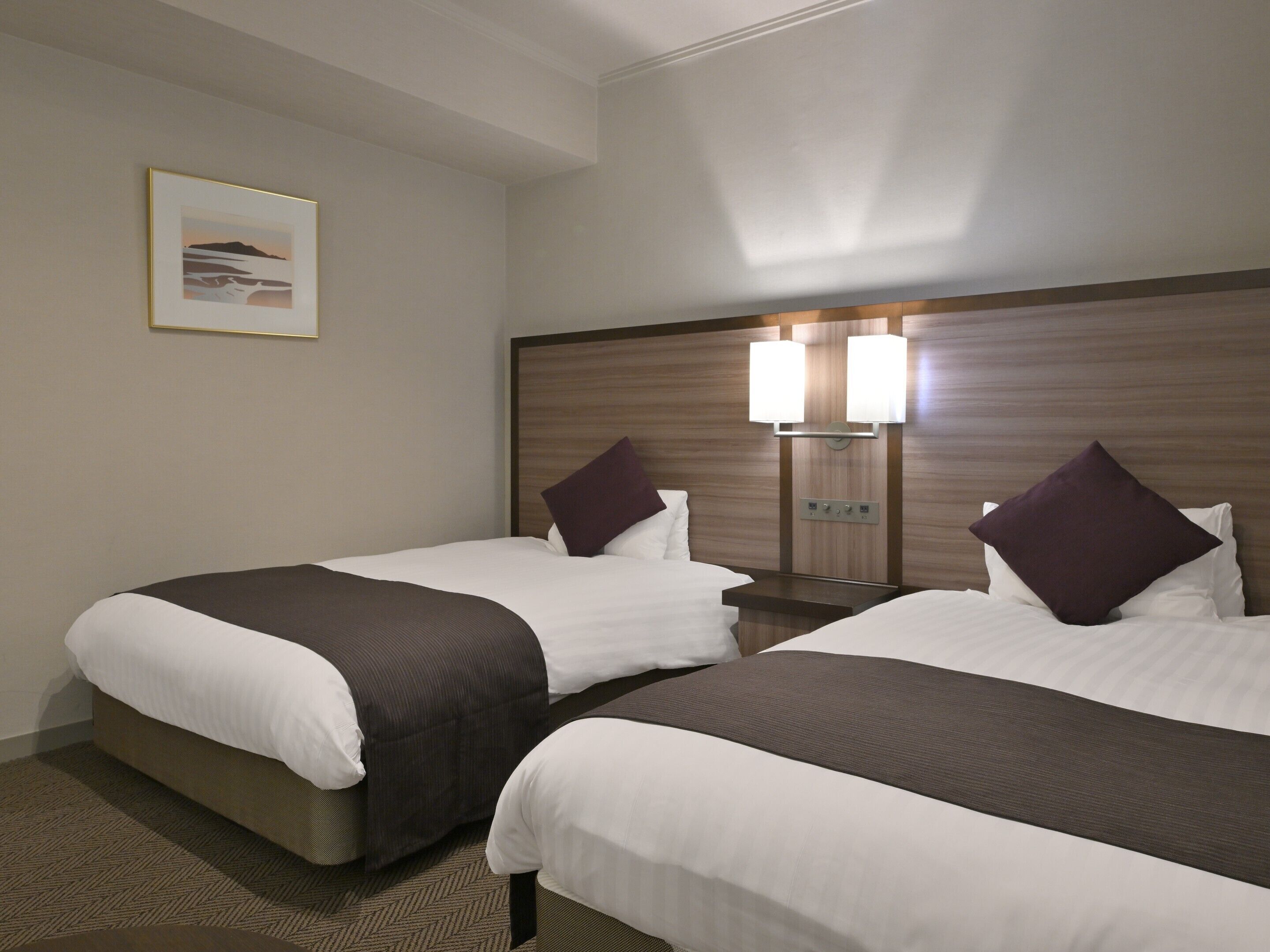 A hotel room with two beds, a headboard with integrated lighting, a framed picture on the wall, and a carpeted floor.