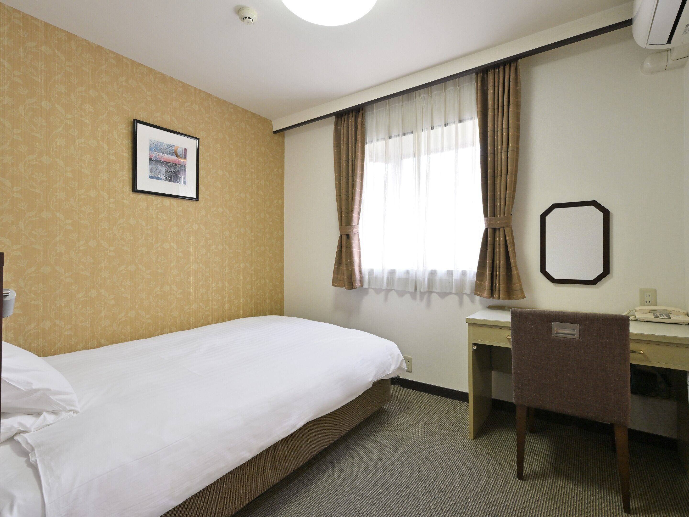 A hotel room with a bed, a desk, a chair, a telephone, and a window with curtains.