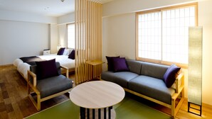 A modern hotel room with a sofa, a small round table, a bed, and a large window.