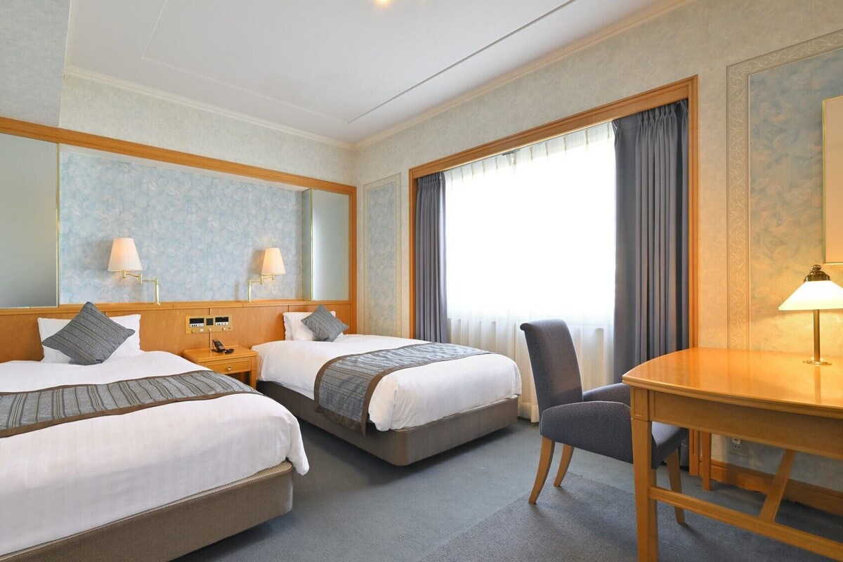 A hotel room with two beds, a desk, and a chair.