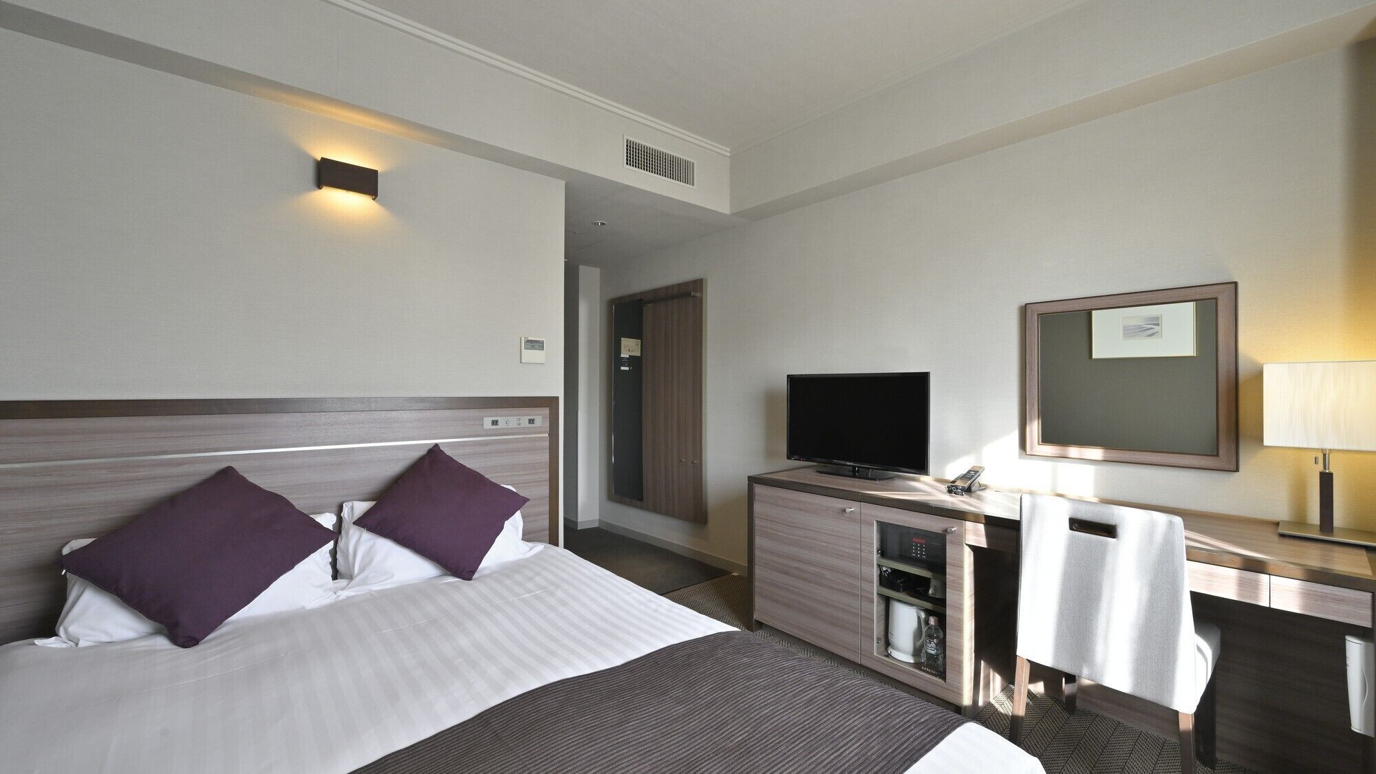 A hotel room with a bed, a TV, a desk, and a mirror.