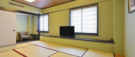Een kamer met tatami matten, een televisie, schuifdeuren en een stoel.
