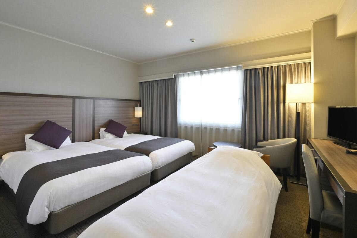A hotel room with two beds, a desk, a chair, a television, and a window with curtains.