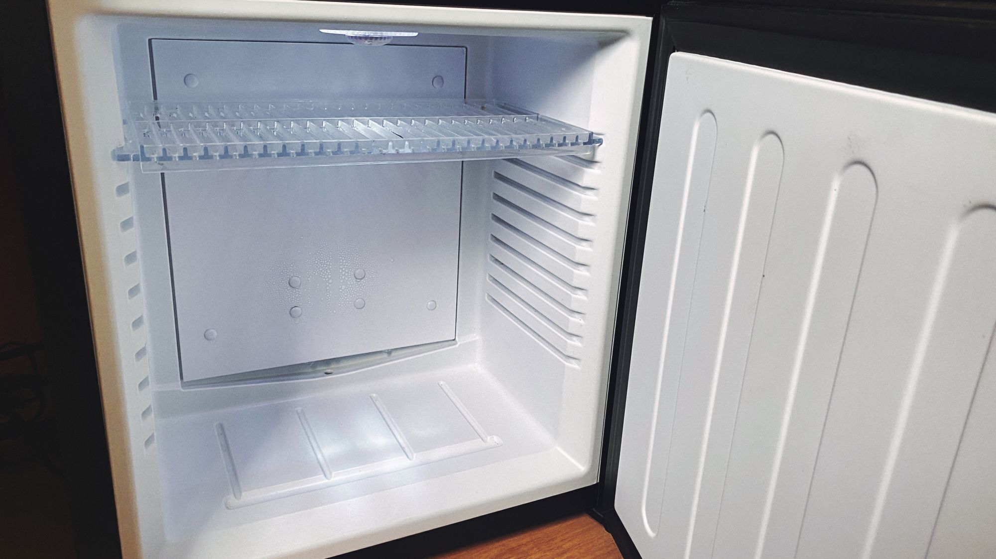 An open refrigerator with a transparent shelf, a freezer compartment, and a water dispenser.