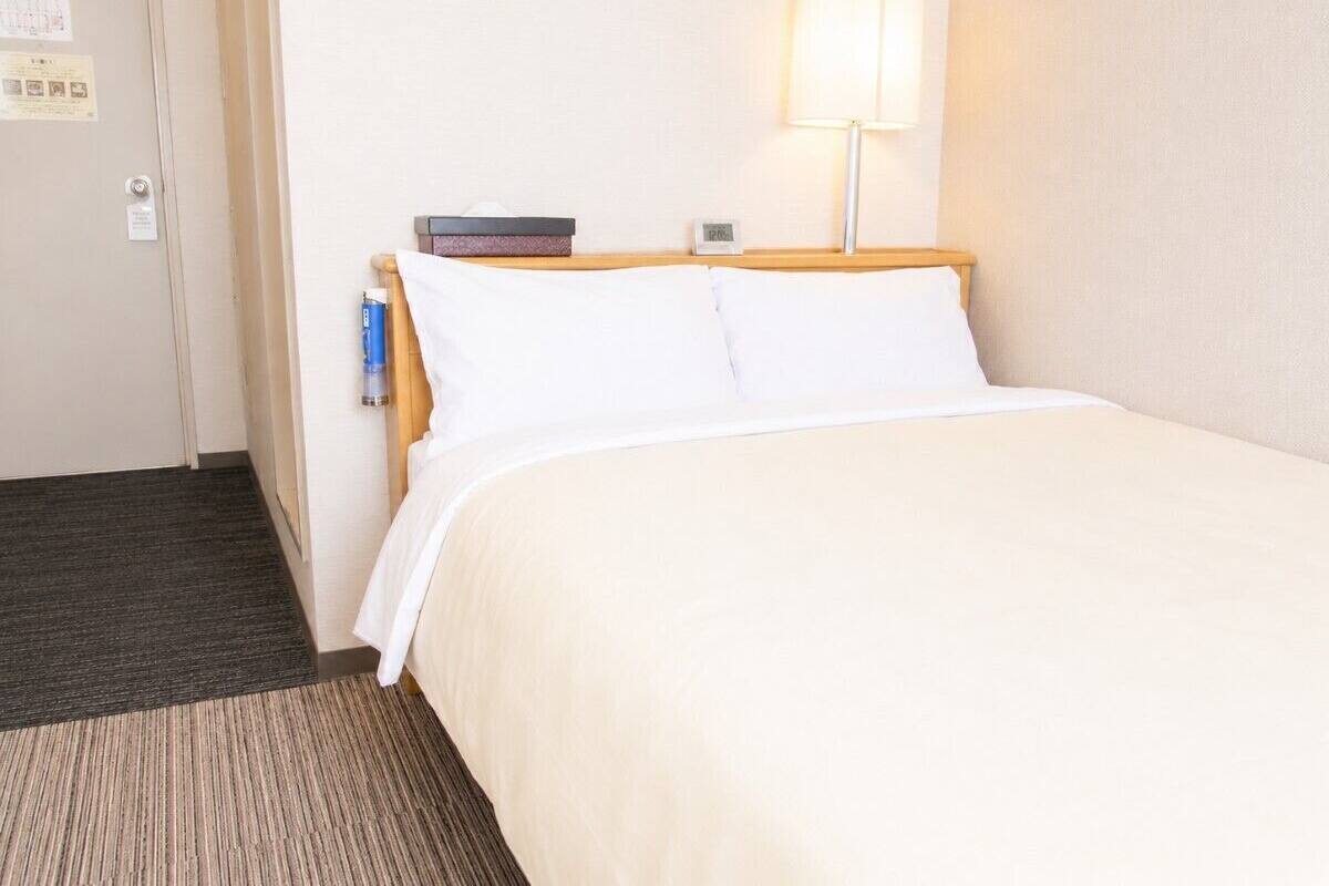 A hotel room with a bed, a nightstand, a lamp, and a door.