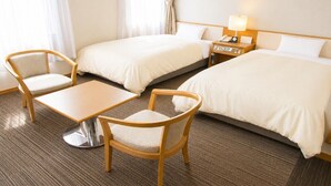 Hotelkamer met twee bedden, een kleintje tafeltje, twee stoelen, een nachtkastje met lamp en een raam met gordijnen.