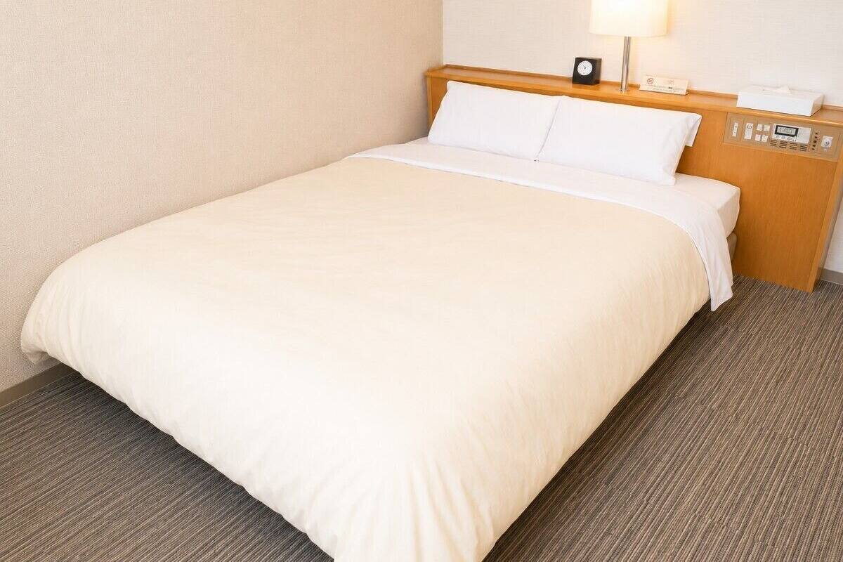 A hotel room with a bed, a nightstand with a lamp, and a control panel.
