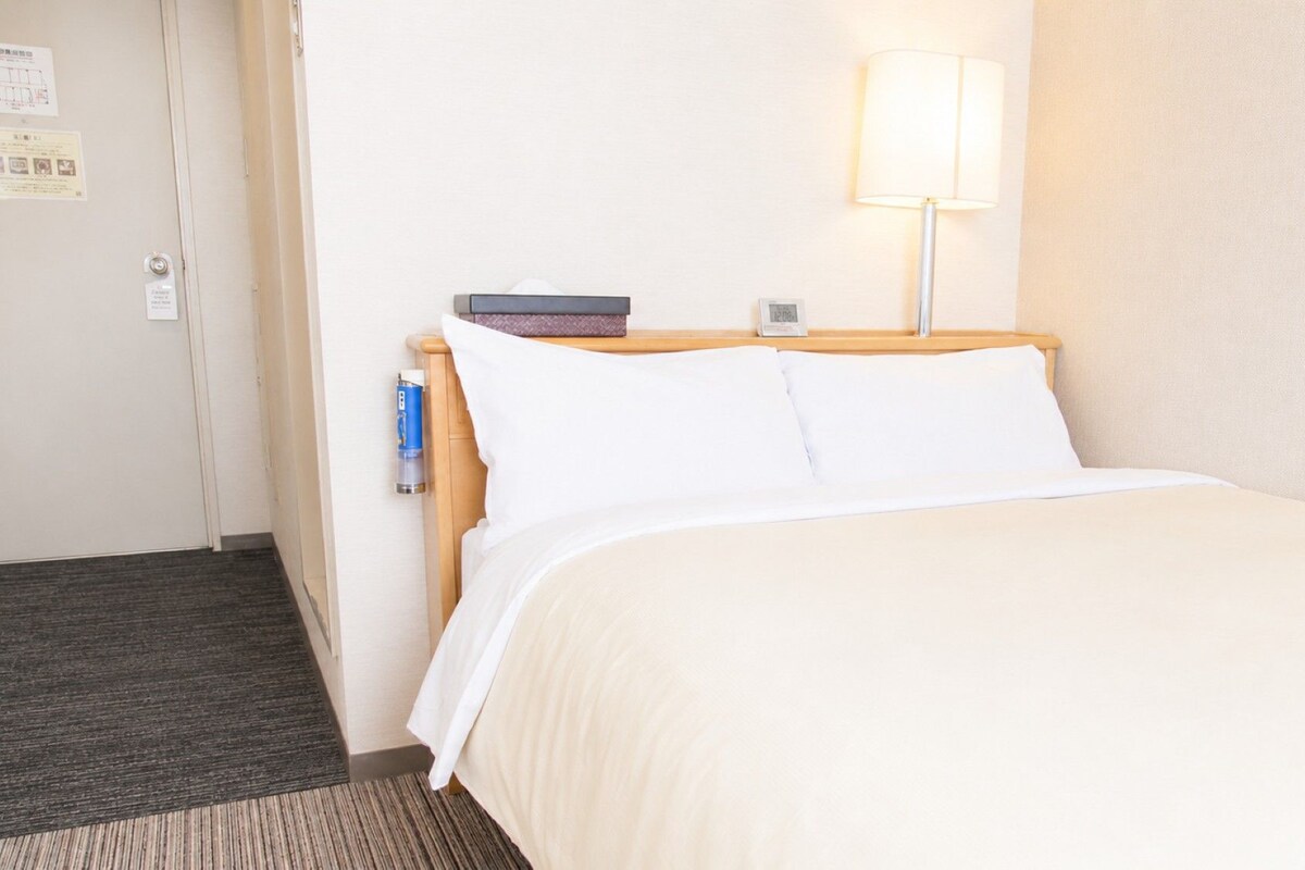 A hotel room with a bed, a bedside table with a lamp, and a wall clock.
