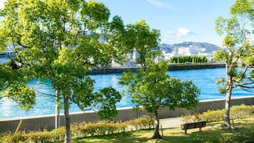 Un parc a la riba del riu, amb arbres, una banca i vista a un paisatge urbà.
