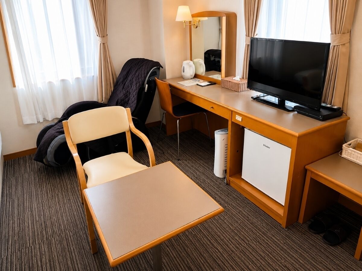 A hotel room with a desk, chair, television, and a mini-fridge.