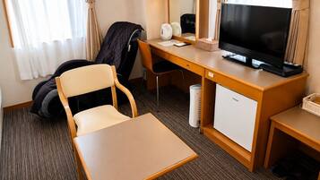 A hotel room with a desk, chair, television, and a mini-fridge.