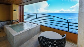 A spa area with a large bathtub, a small table, and a wicker chair, overlooking a body of water with a railing. - Hokkawa Onsen Hotel (Higashiizu)