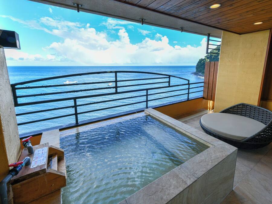 A balcony with a view of the sea, a small pool, and a wicker chair.