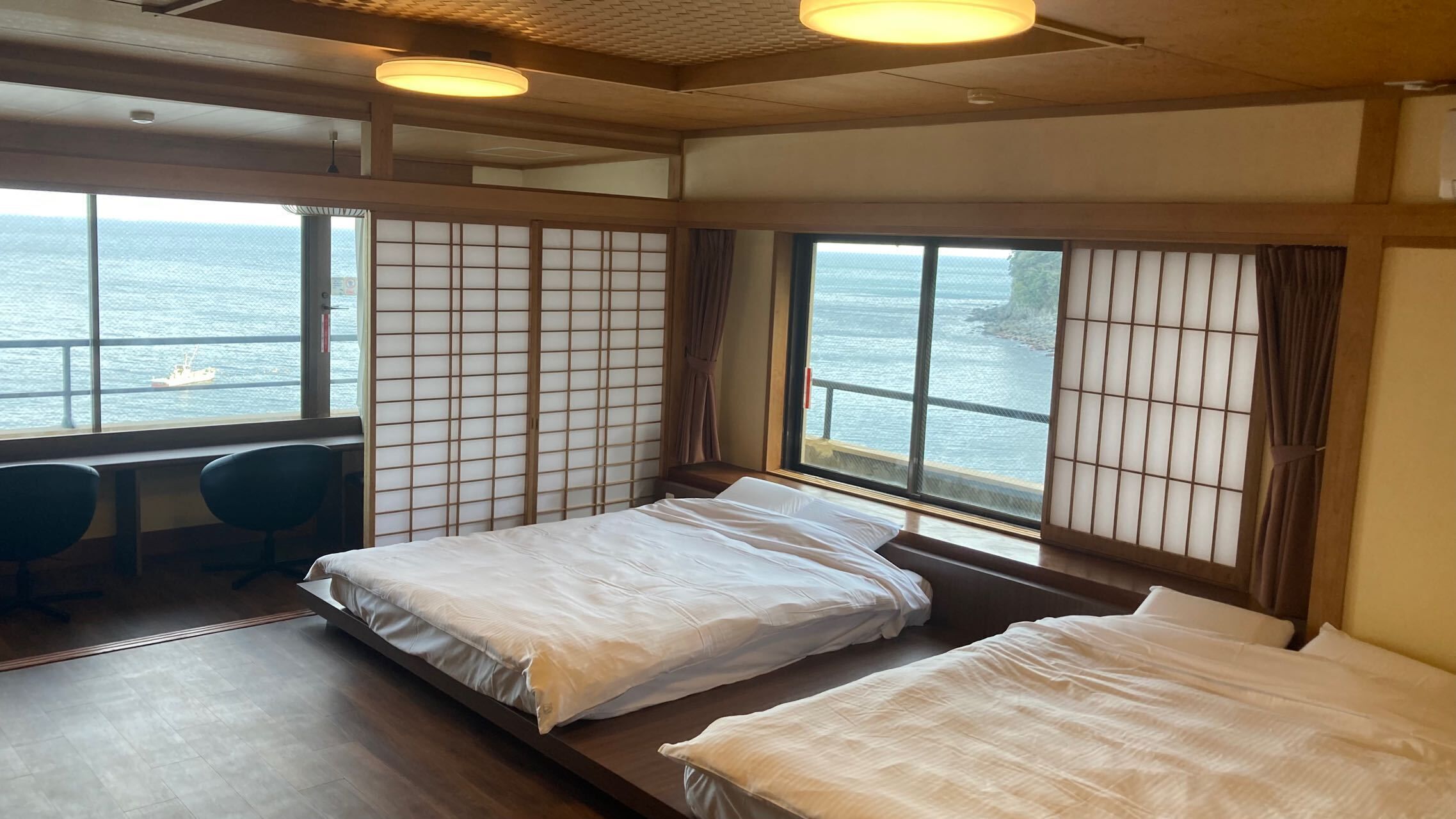 A room with two beds, a desk, and a view of the sea.
