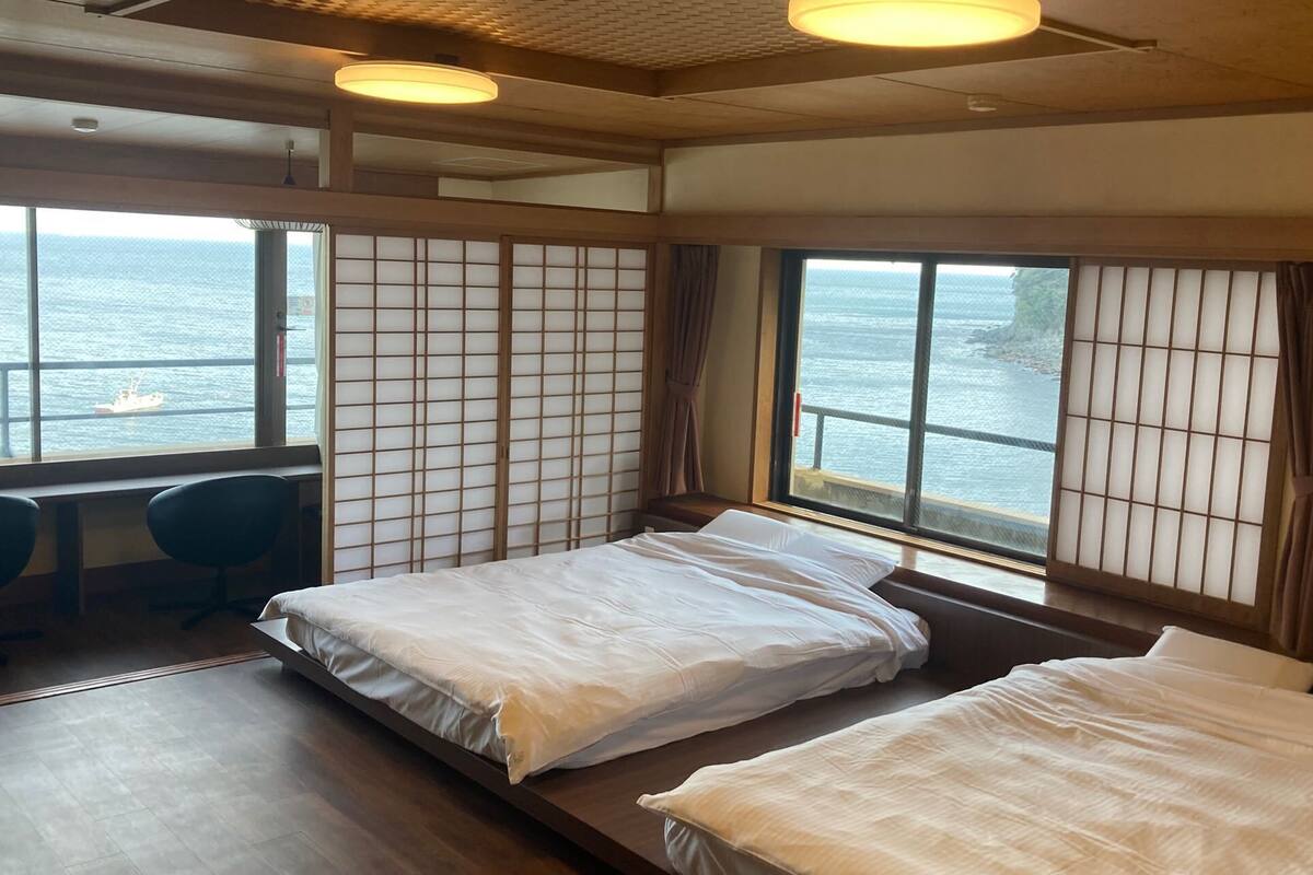 Una habitación con dos camas, un escritorio y vista al mar.