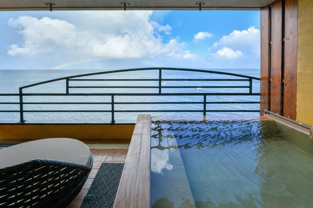 Un balcón con vista al mar y un arcoíris, una terraza de madera y una zona con cerramiento de vidrio.