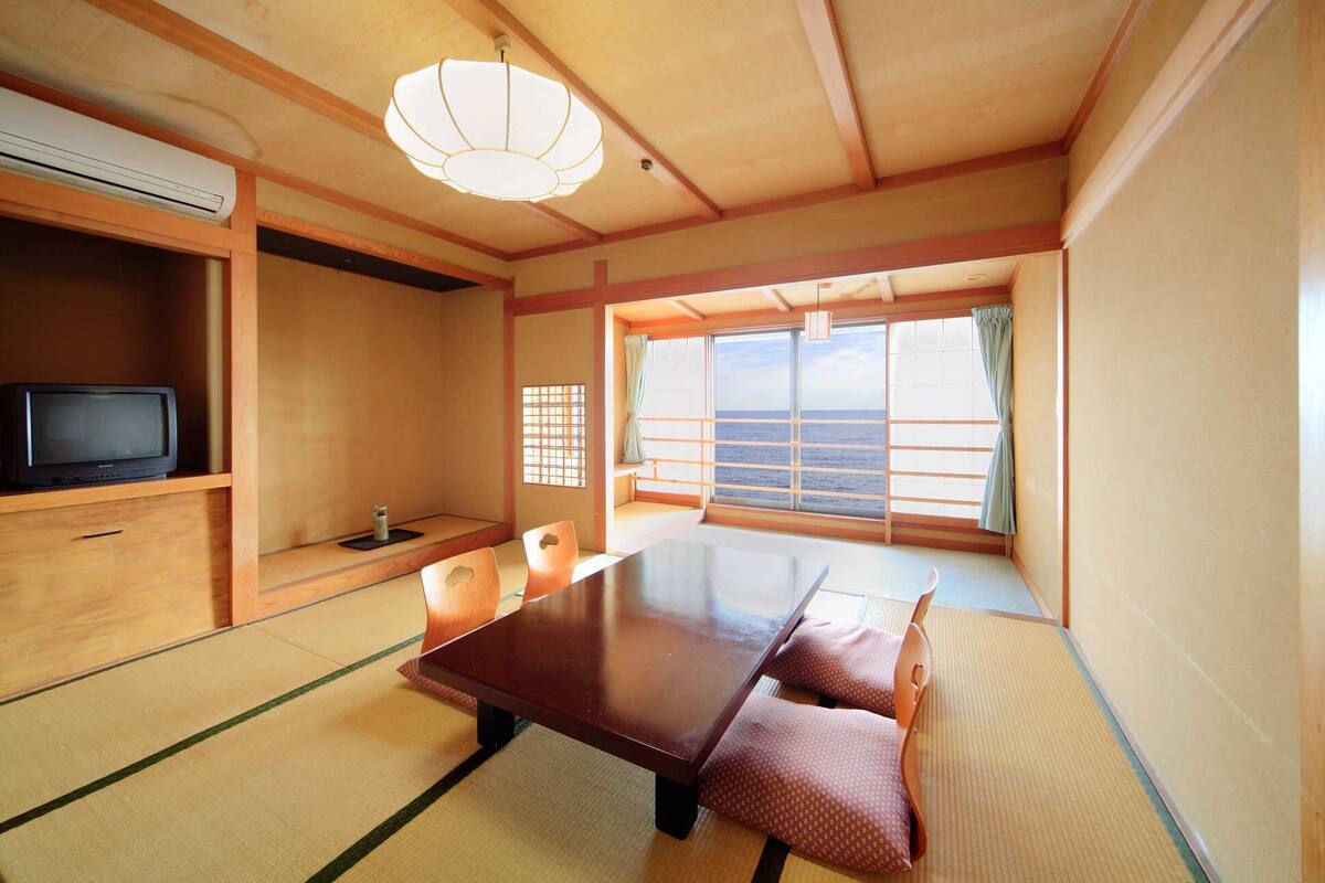 Una habitación japonesa tradicional con suelo de tatami, una mesa baja, cojines, un televisor y vistas al mar.