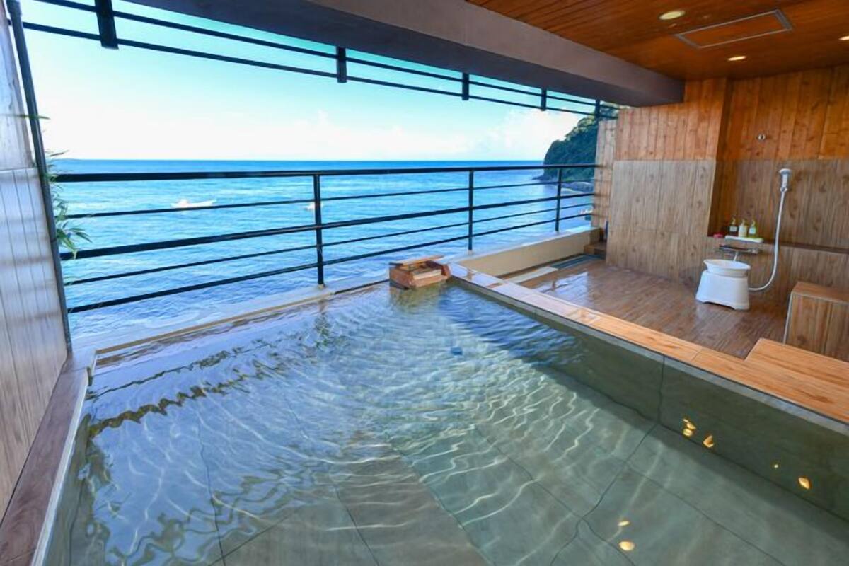 Piscina interior moderna con agua cristalina, suelo de madera, un banco de madera y vistas al océano.