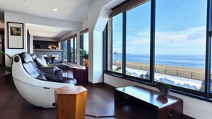 A modern room with a massage chair, a wooden side table, and a view of the beach. - Hokkawa Onsen Hotel (Higashiizu)