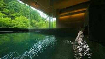 A pool with clear water, surrounded by a glass wall, and a view of green trees outside.