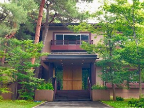 A modern two-story building with a balcony, surrounded by lush greenery.