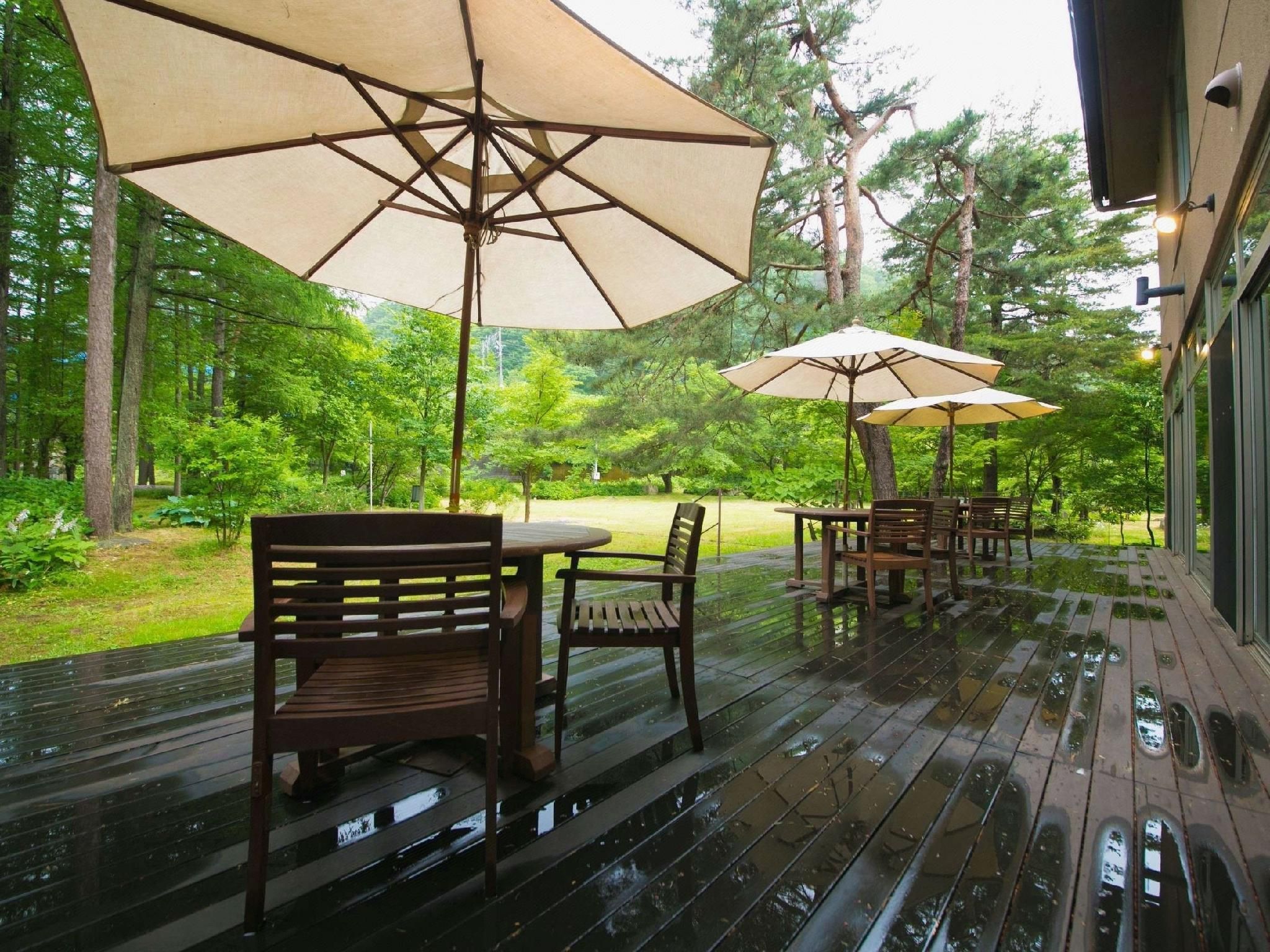 An outdoor deck with wooden furniture and large umbrellas, surrounded by trees.