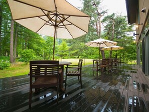 Une terrasse extérieure avec des meubles en bois et de grands parasols, entourée d’arbres.