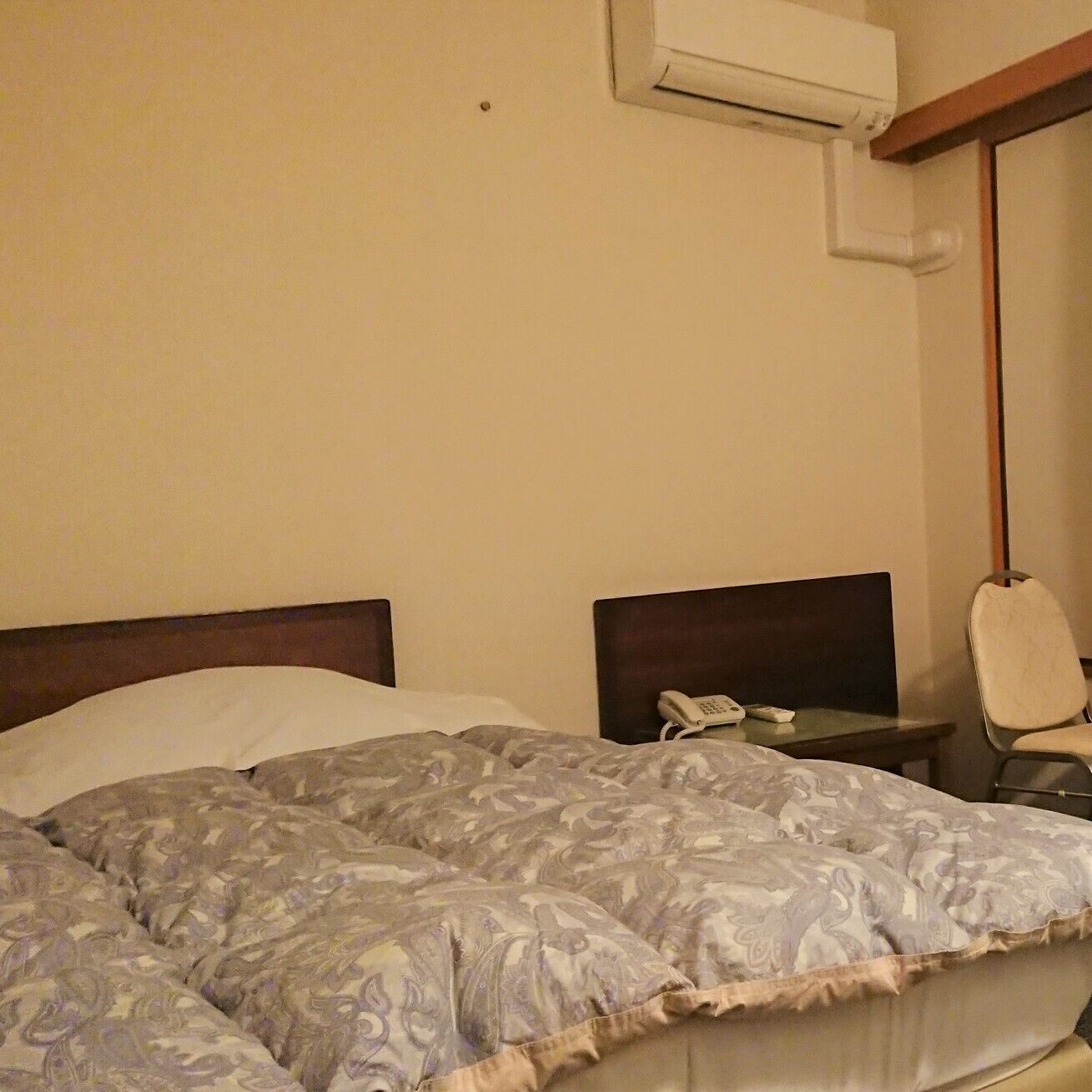 Et hotelværelse med en seng, et natbord med en telefon og en aircondition-enhed på væggen.
