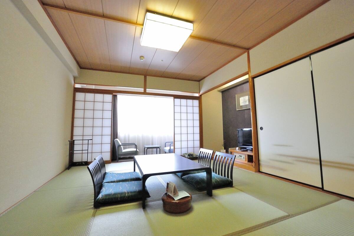 Ein traditioneller japanischer Raum mit Tatami-Böden, einem niedrigen Tisch, Kissen und verschiebbaren Türen.