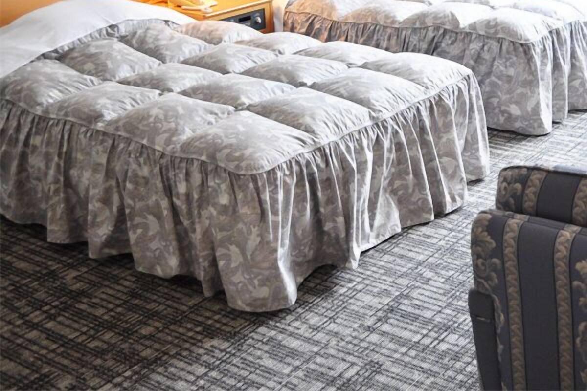 Ein Hotelzimmer mit zwei Betten, einem Nachttisch mit Lampe und einem gemusterten Teppich.