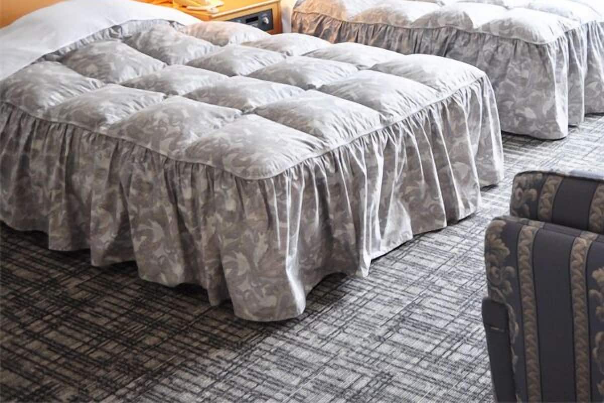A hotel room with two beds, a nightstand with a lamp, and a patterned carpet.