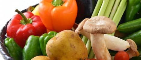 Een mand gevuld met diverse groenten, waaronder rode en groene paprika’s, tomaten, champignons en aardappelen.