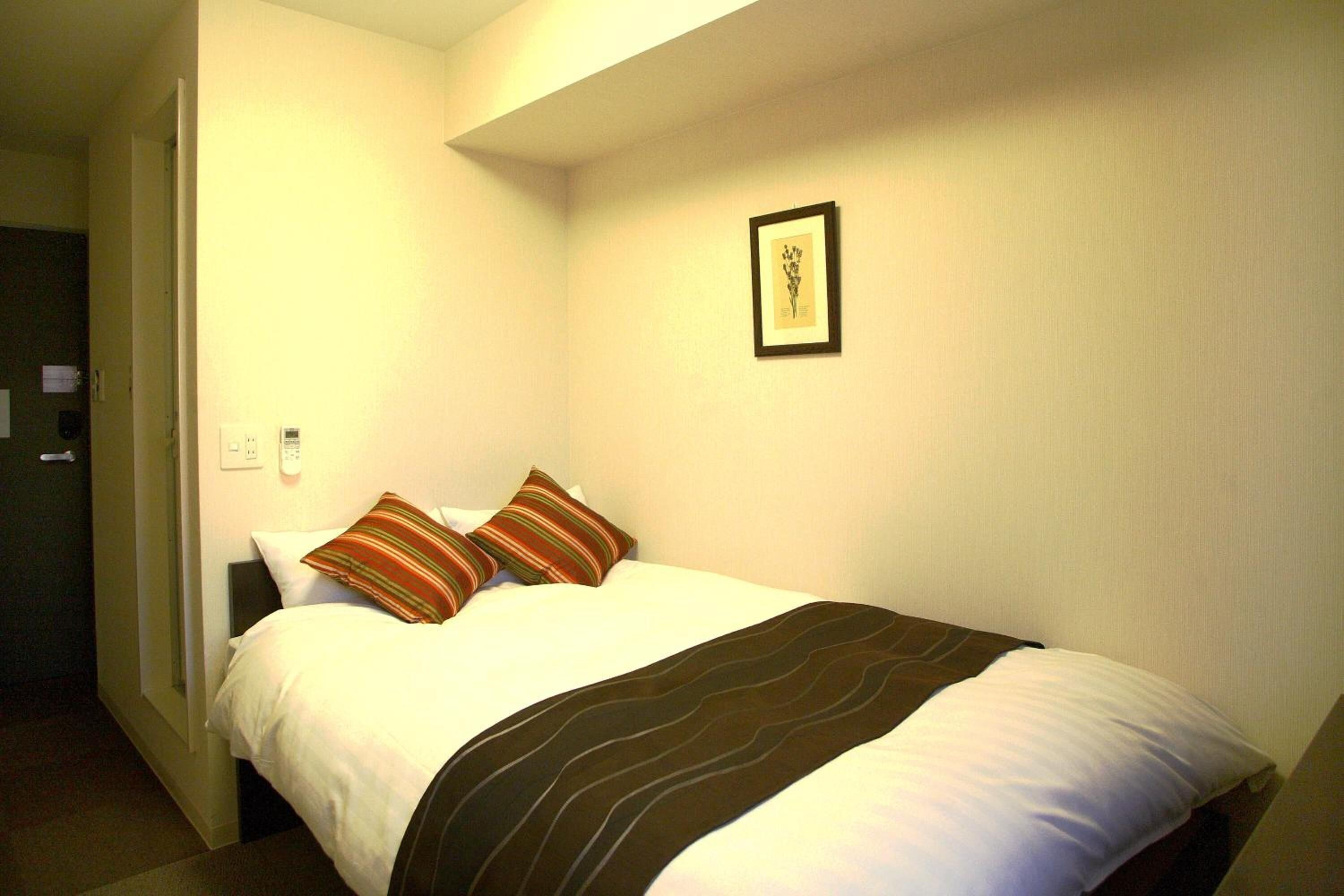 Habitación de hotel con cama, dos almohadas, un cuadro en la pared y una puerta que da a otra habitación.