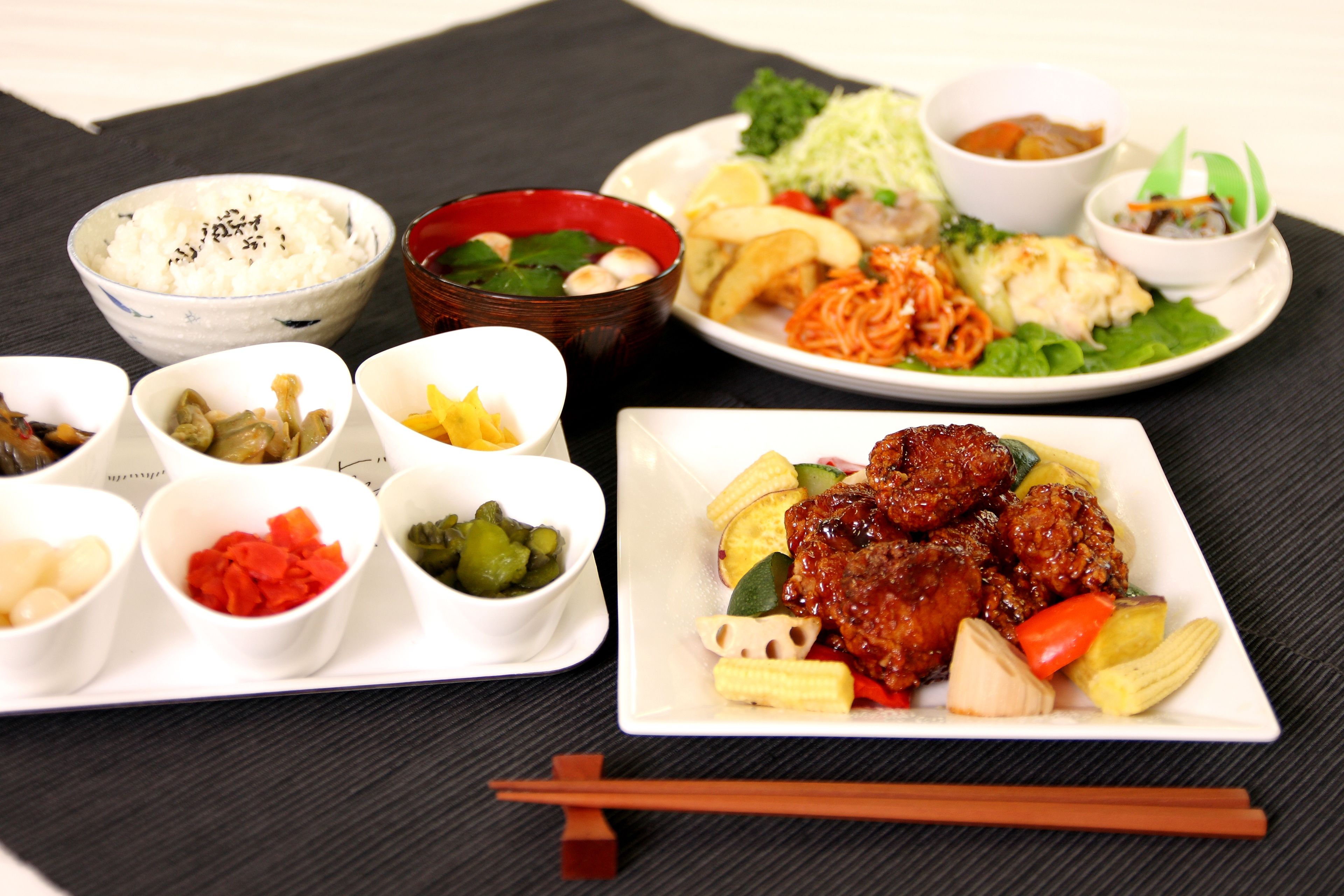 Diversos platos que incluyen arroz, verduras y carne, sobre un mantel negro con palillos.