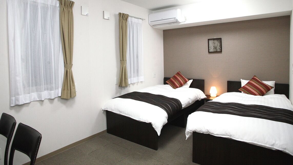 A hotel room with two beds, a desk, and a chair.