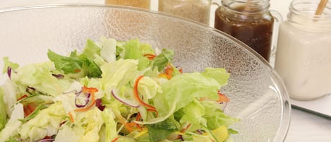 Uma taça de vidro transparente com salada mista e diversos vegetais, sobre um fundo de toalha de mesa branca.