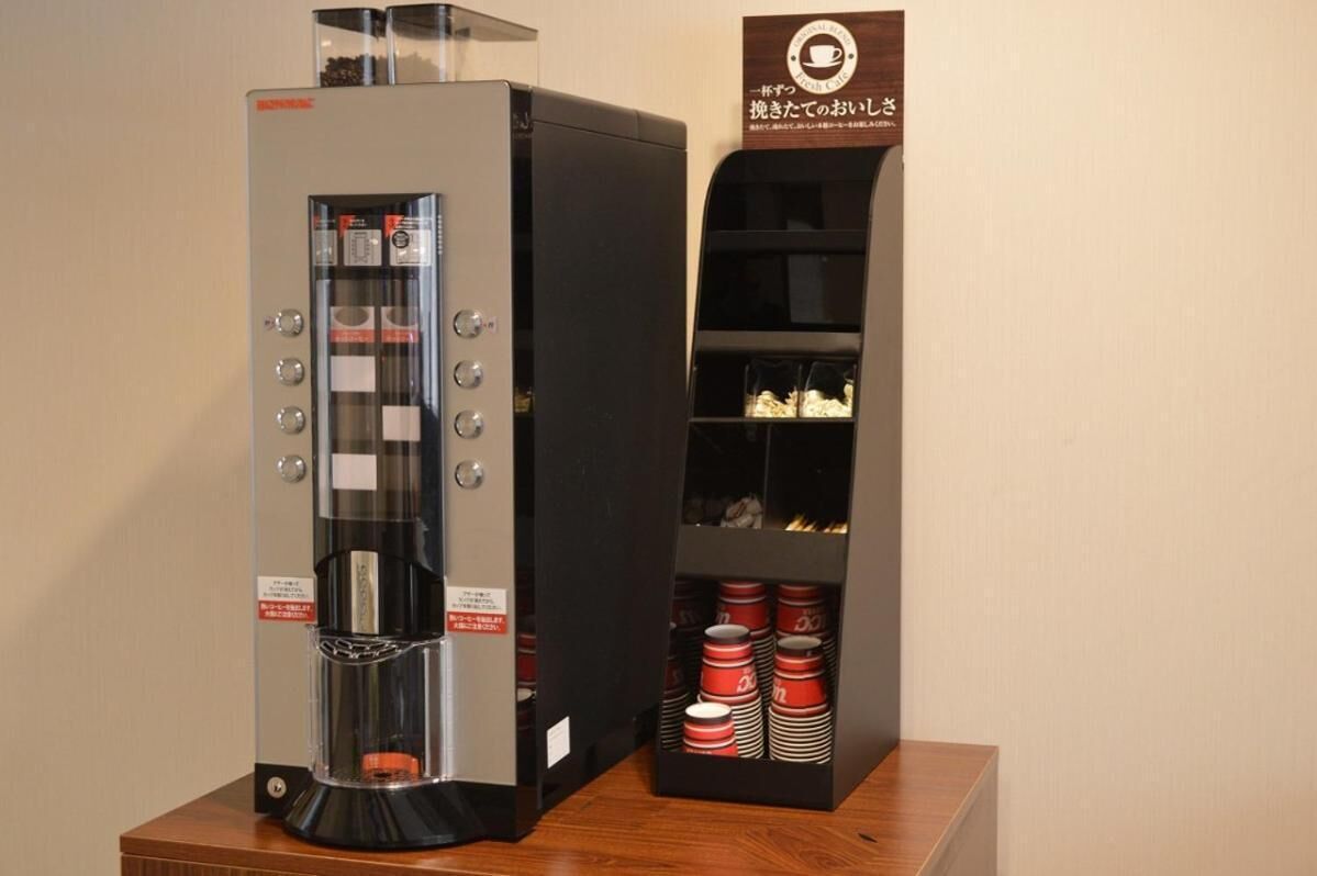 Une machine à café avec une façade en verre et des boutons, placée à côté d’une vitrine contenant des tasses rouges et blanches.