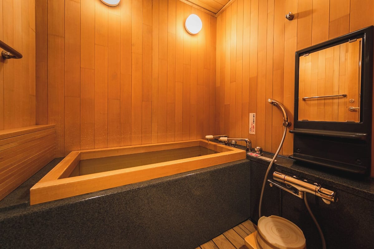 A wooden interior with a bathtub, a toilet, and a mirror.