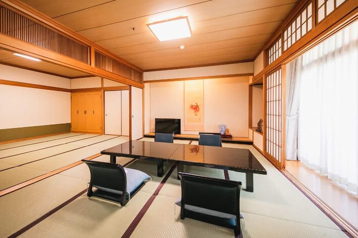 A traditional Japanese room with tatami flooring, a low table with chairs, a television, and sliding doors.