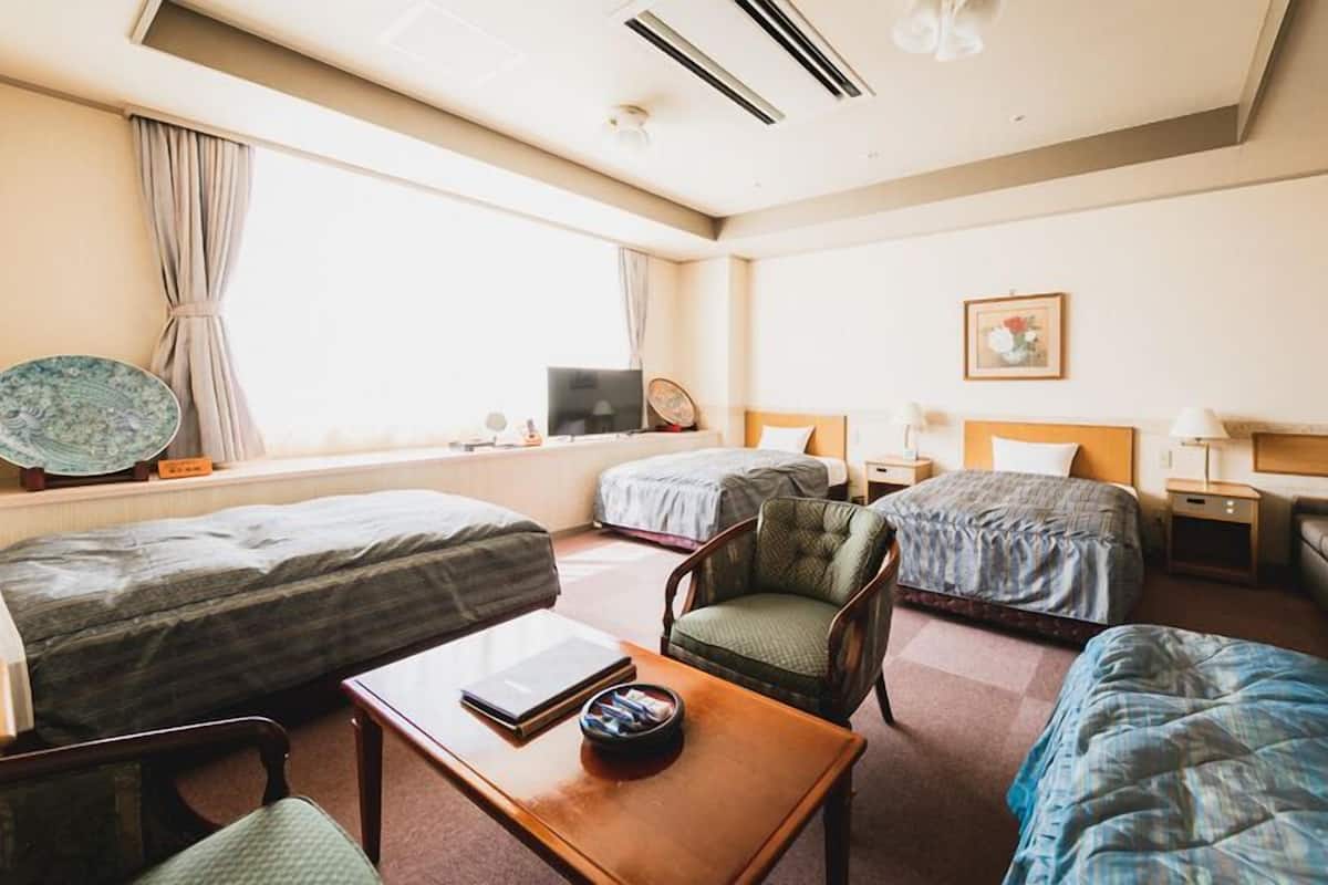 A hotel room with two single beds, a sofa, a chair, a small table, and a television.