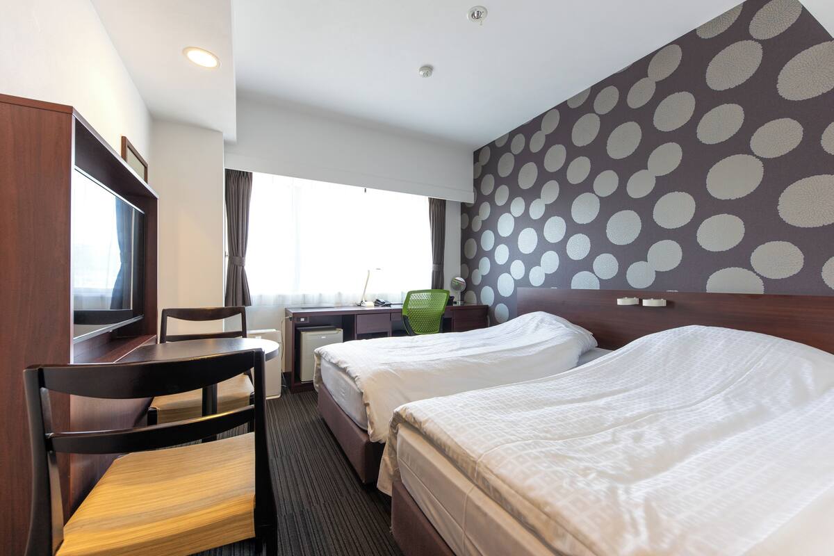 A hotel room with two beds, a desk, a chair, a television, and a window with curtains.