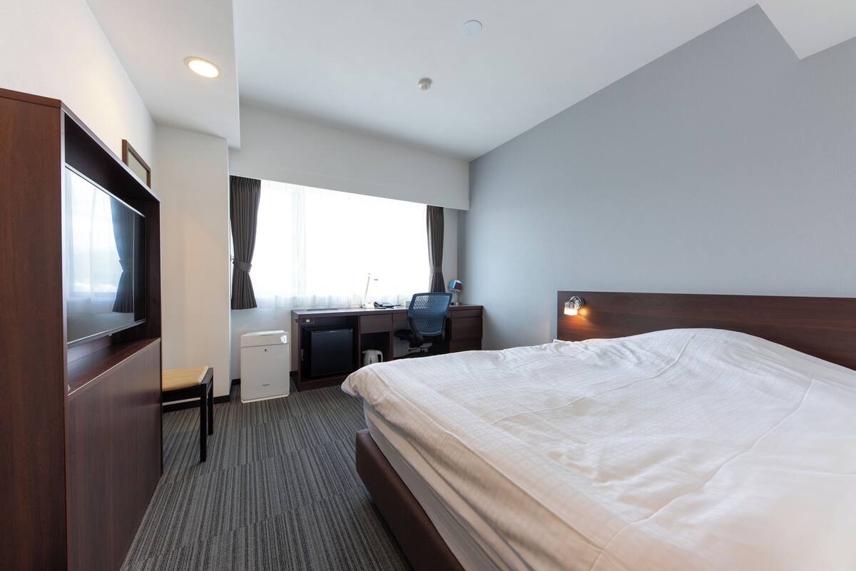 A hotel room with a bed, desk, chair, and a television.