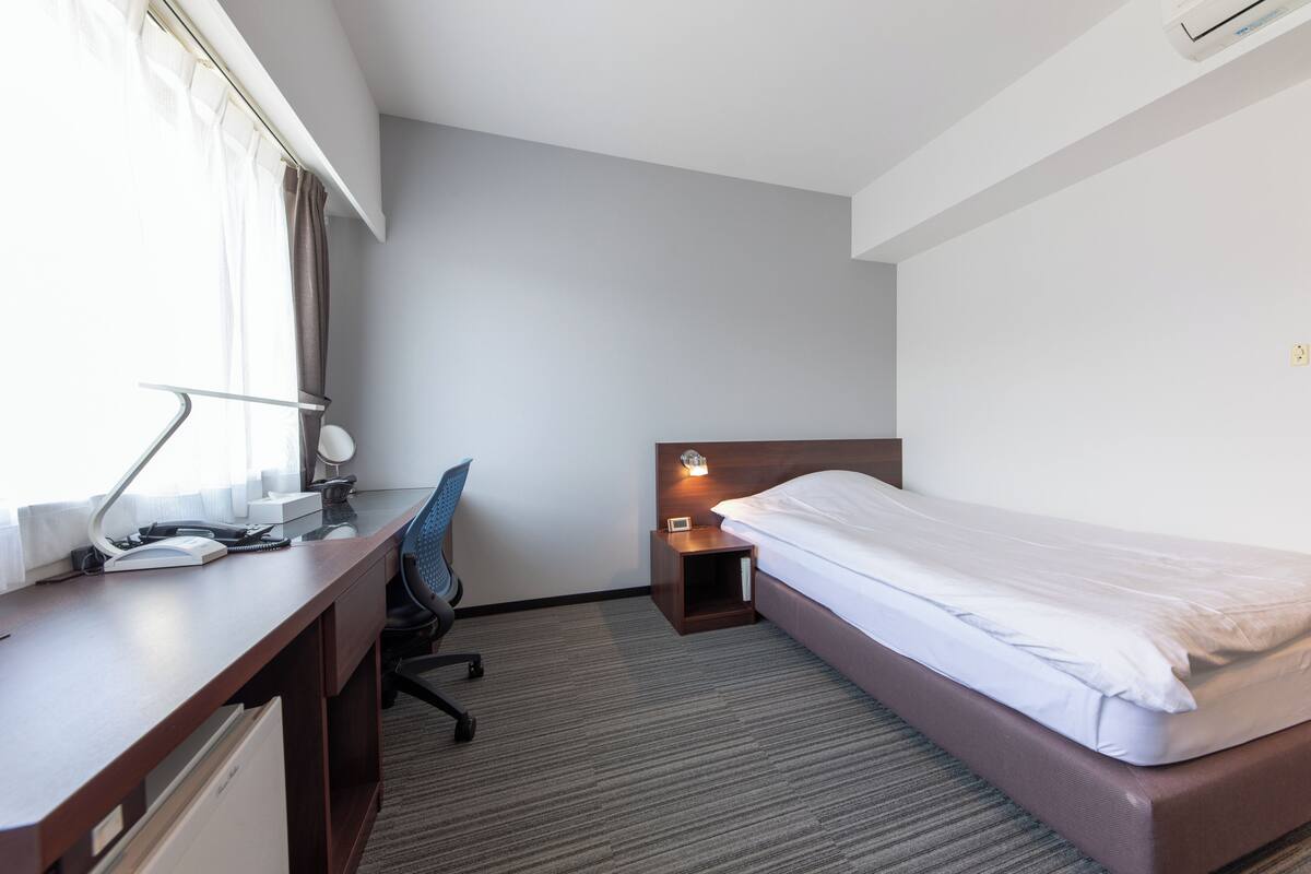 A hotel room with a bed, desk, chair, and bedside table.