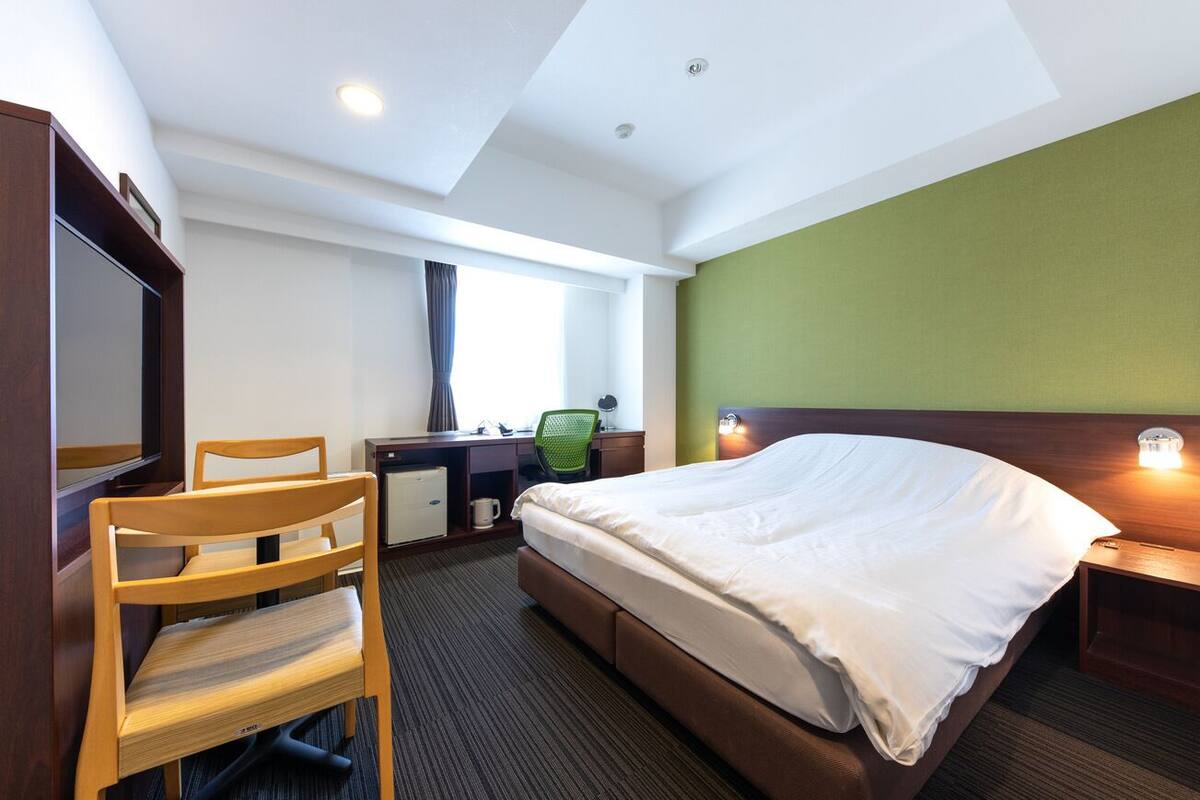 A hotel room with a bed, desk, chair, and a television.